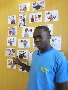 Sanergy team member Oliver in Sanergy's office, gesturing towards his I Am Kenyan portrait